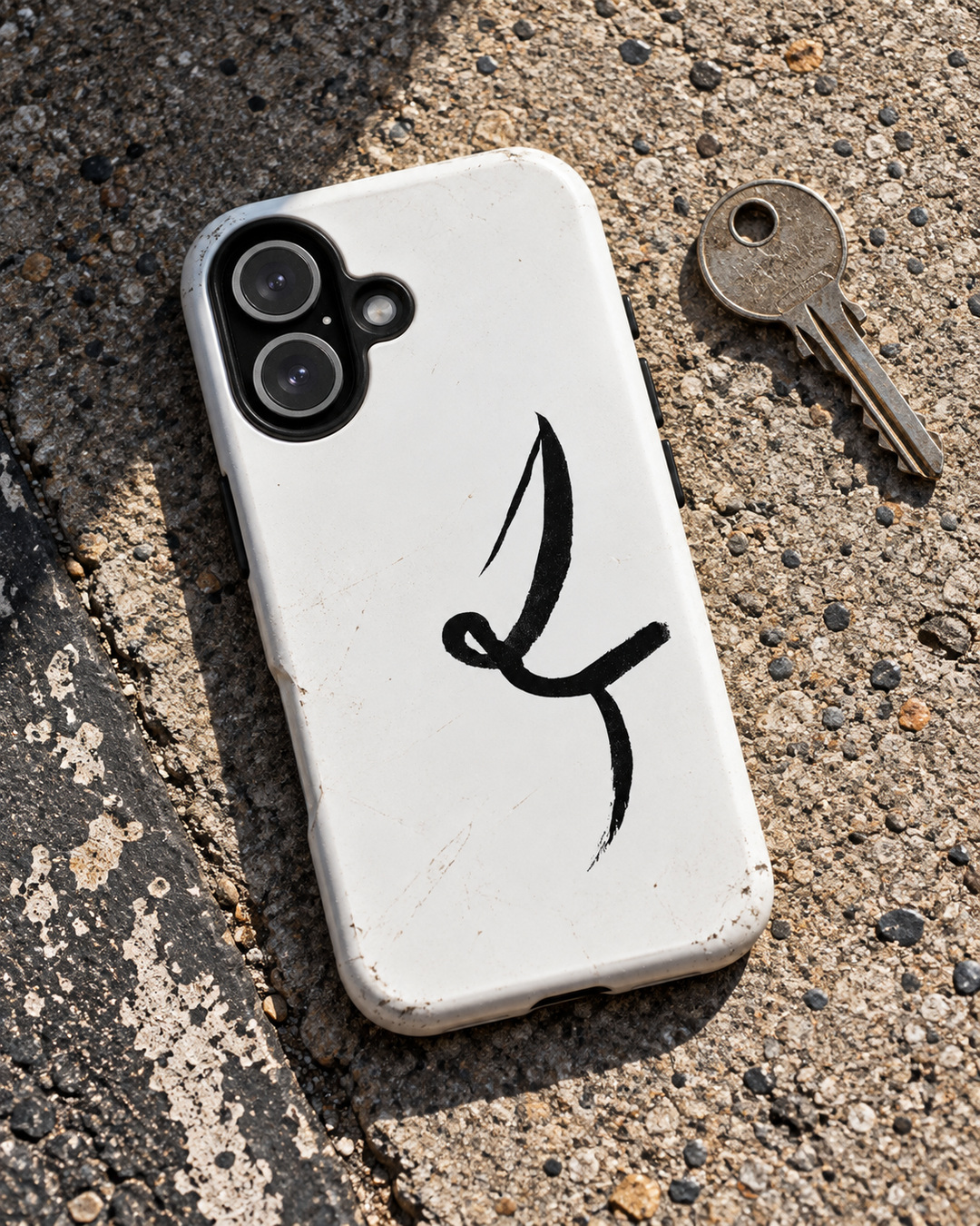 White One Line phone case with black ink mark, resting beside a key on sunlit concrete