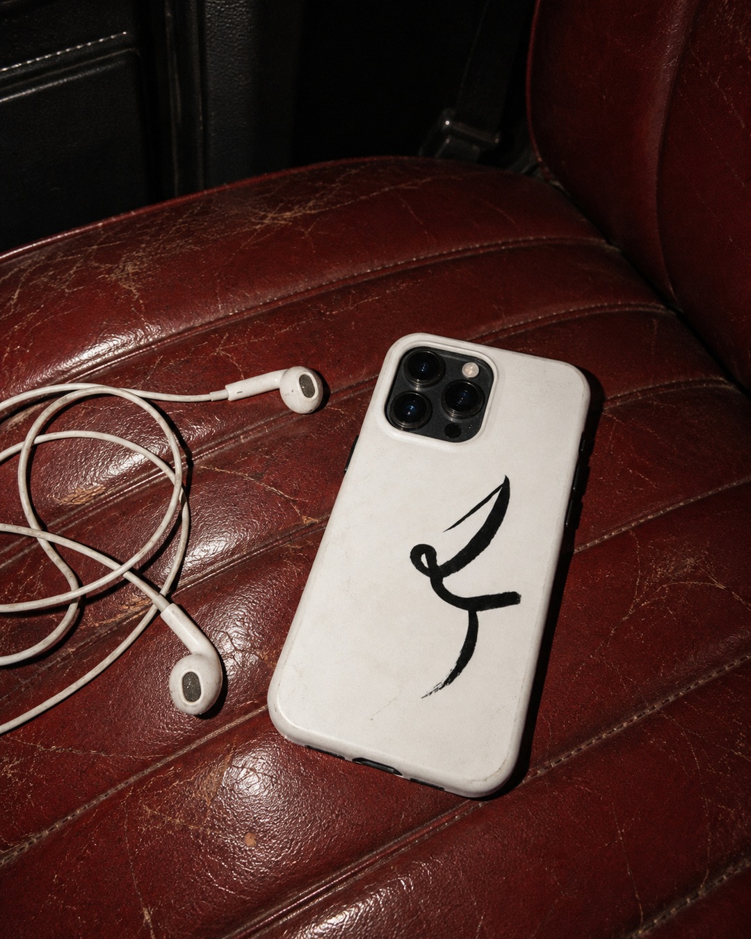 White One Line phone case with black ink drawing beside tangled earbuds on a worn red car seat