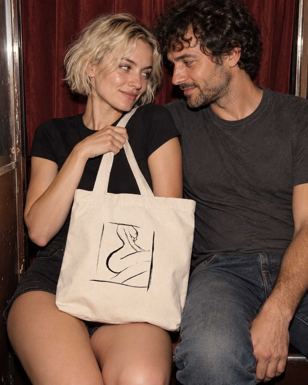 Natural canvas Full Boon tote with black ink drawing held between two adults in a burgundy photo booth