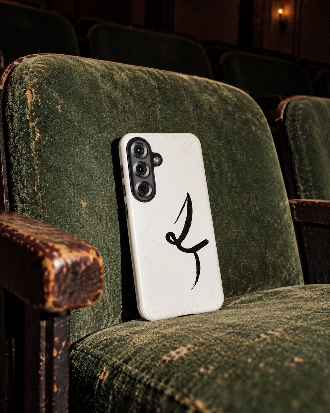 White One Line phone case with black curved ink mark propped against worn green velvet cinema seat
